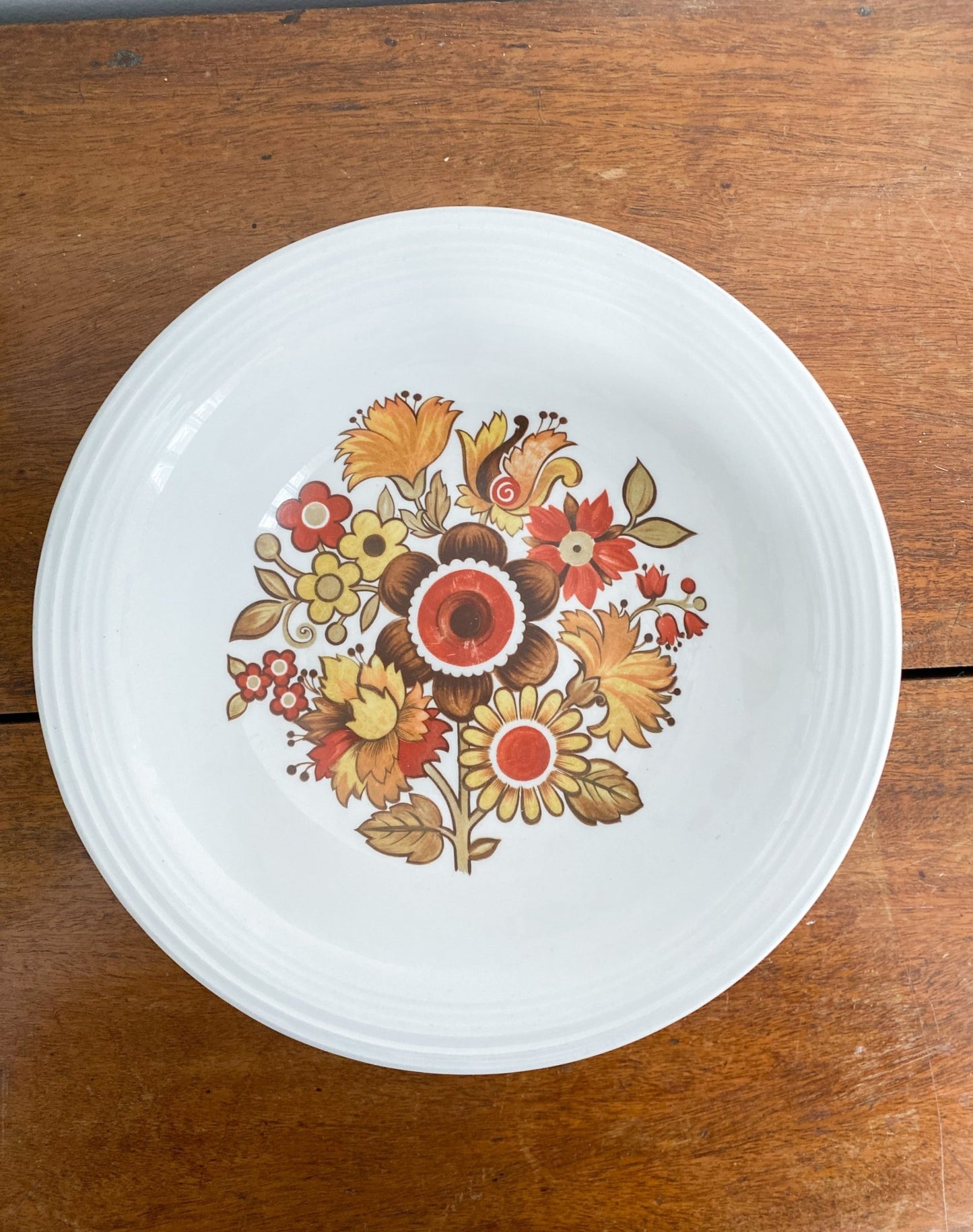 The bowl is sitting on the table, and the camera is facing the inside with the inside of the bowl showing. The inner bowl has a scene of many flowers in different variations and colours ranging in red, yellow and orange.