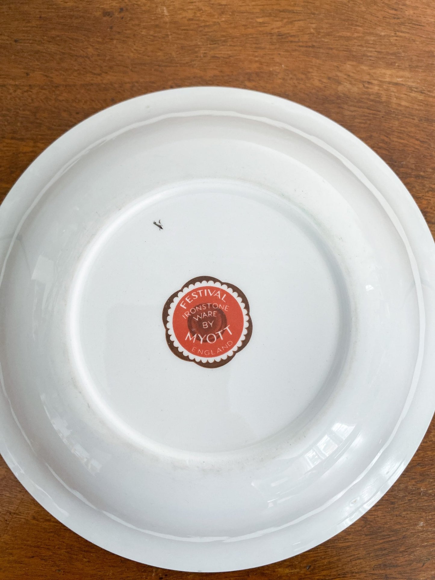 The bowl is sitting on the table upside down showing the red and brown maker's stamp, "Ironstone Ware by Myott, Fesitival"