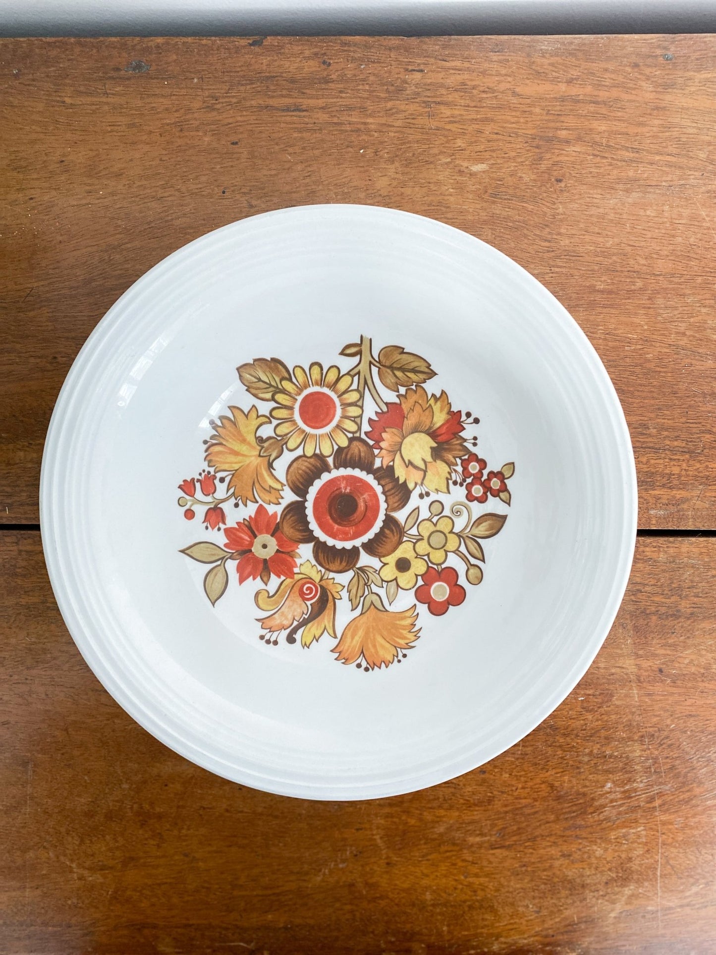 The bowl is sitting on the table, and the camera is facing the inside with the inside of the bowl showing. The inner bowl has a scene of many flowers in different variations and colours ranging in red, yellow and orange.